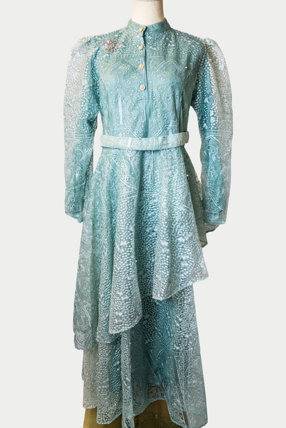 A stunning long layered dress in green with pearls and delicate embroidery. The dress has mandarin collar, buttons, long sleeves, and is fully lined. There are hidden zips at the back and sleeves for ease of wear. The design is hijabi-friendly for modesty and style. It also includes a size-adjustable belt for a customized fit.