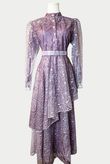 A stunning long layered dress in purple with delicate embroidery. The dress has mandarin collar, buttons, long sleeves, and is fully lined. There are hidden zips at the back and sleeves for ease of wear. The design is hijabi-friendly for modesty and style. It also includes a size-adjustable belt for a customized fit.