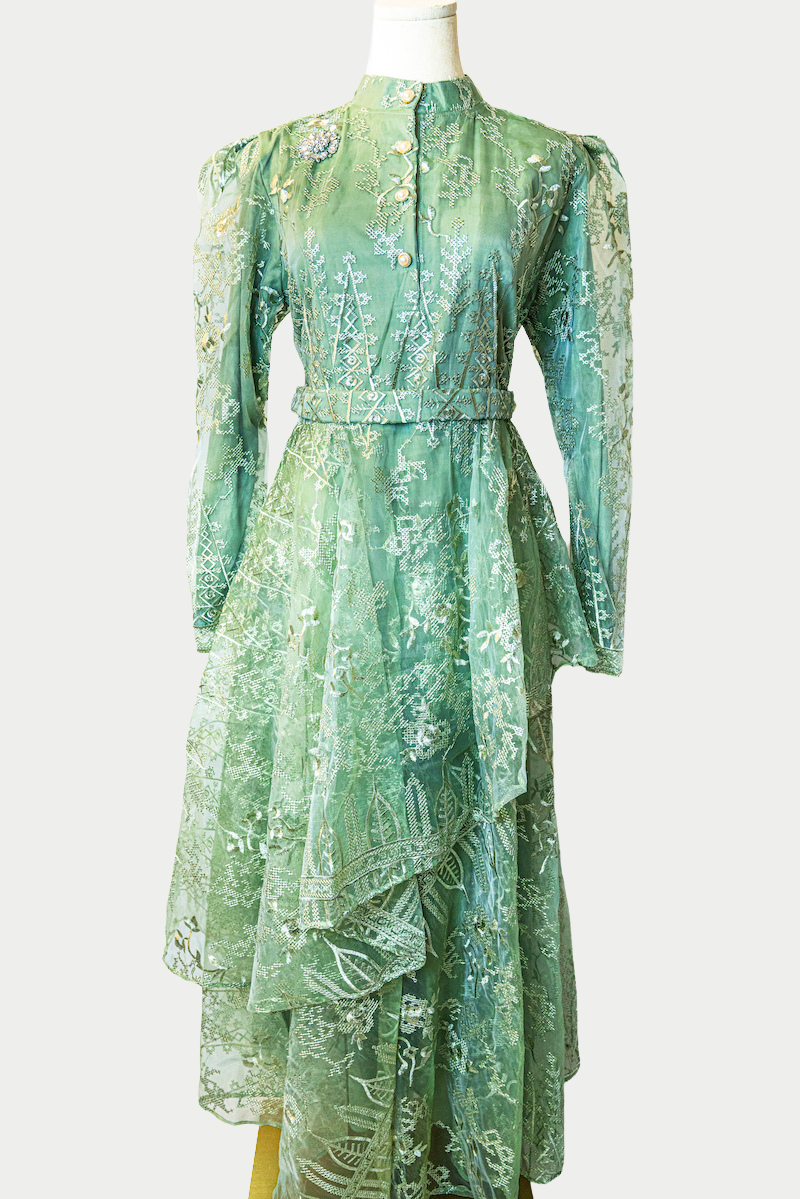 A stunning long layered dress in green with delicate embroidery. The dress has mandarin collar, buttons, long sleeves, and is fully lined. There are hidden zips at the back and sleeves for ease of wear. The design is hijabi-friendly for modesty and style. It also includes a size-adjustable belt for a customized fit.
