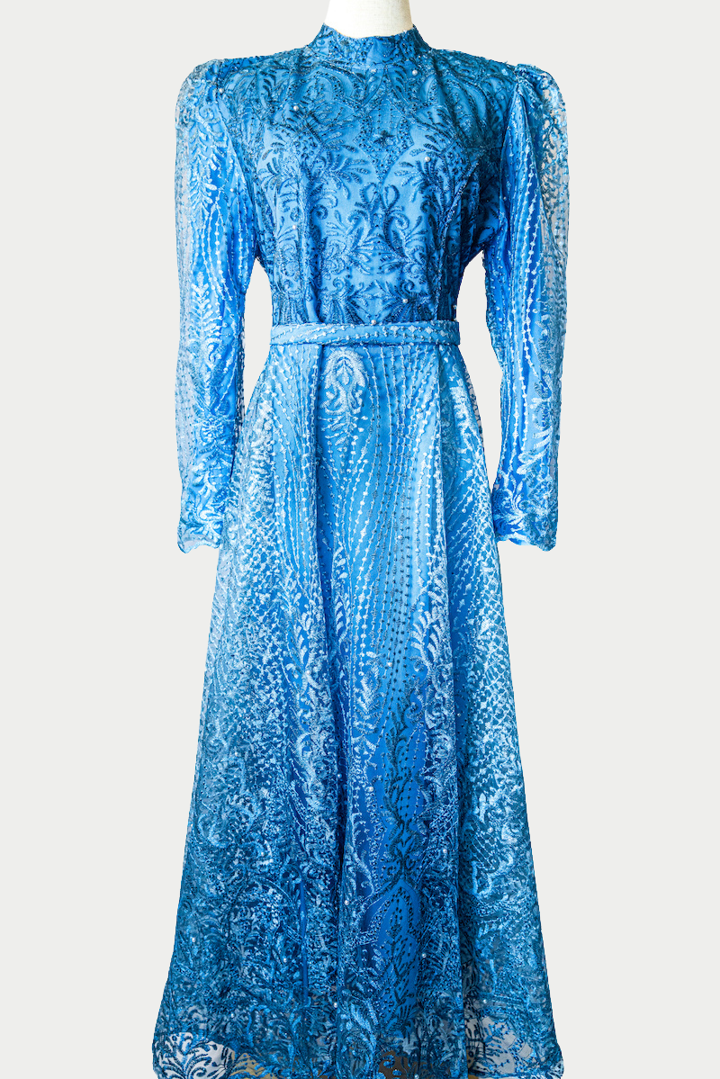 A stunning long dress in blue with pearls and delicate embroidery. The dress has mandarin collar, long sleeves, and is fully lined. There are hidden zips at the back and sleeves for ease of wear. The design is hijabi-friendly for modesty and style. It also includes a size-adjustable belt for a customized fit.