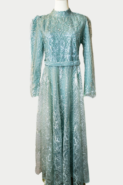 A stunning long dress in green with pearls and delicate embroidery. The dress has mandarin collar, long sleeves, and is fully lined. There are hidden zips at the back and sleeves for ease of wear. The design is hijabi-friendly for modesty and style. It also includes a size-adjustable belt for a customized fit.
