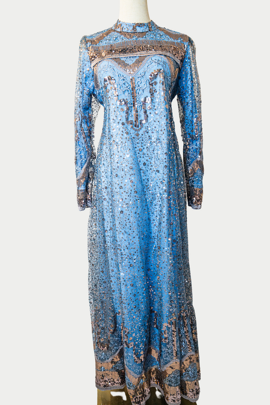 A stunning long dress in green with sequins and delicate embroidery. The dress has mandarin collar, long sleeves, and is fully lined. There are hidden zips at the back and sleeves for ease of wear. The design is hijabi-friendly for modesty and style. It also includes a size-adjustable belt for a customized fit.