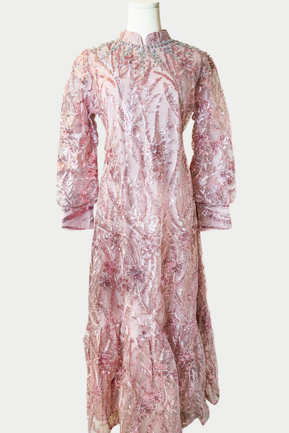 A stunning long dress in pink with sequins and delicate embroidery. The dress has mandarin collar, banded cuffs, long sleeves, and is fully lined. There are hidden zips at the back and sleeves for ease of wear. The design is hijabi-friendly for modesty and style. It also includes a size-adjustable belt for a customized fit.