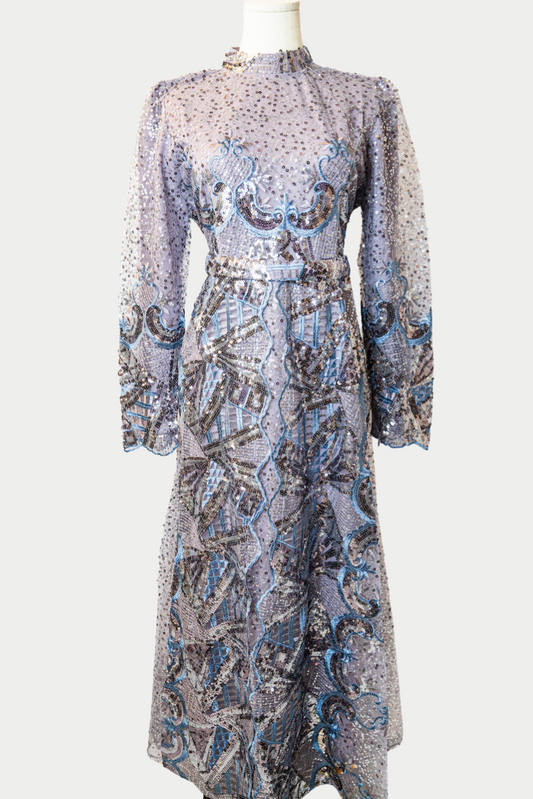 A stunning long dress in purple with sequins and delicate blue embroidery. The dress has mandarin collar, long sleeves, and is fully lined. There are hidden zips at the back and sleeves for ease of wear. The design is hijabi-friendly for modesty and style. It also includes a size-adjustable belt for a customized fit.