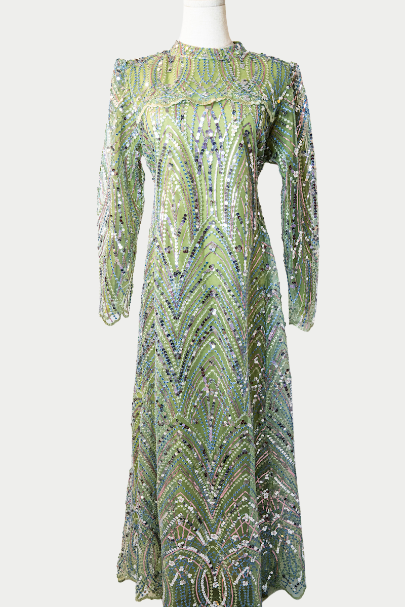 A stunning long dress in green with sequins and delicate embroidery. The dress has mandarin collar, long sleeves, and is fully lined. There are hidden zips at the back and sleeves for ease of wear. The design is hijabi-friendly for modesty and style. It also includes a size-adjustable belt for a customized fit.