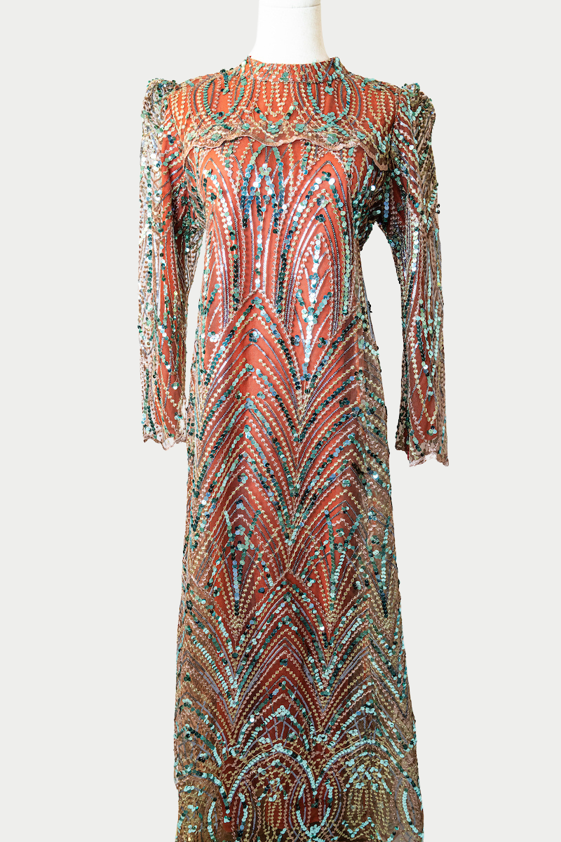 A stunning long dress in orange with sequins and delicate embroidery. The dress has mandarin collar, long sleeves, and is fully lined. There are hidden zips at the back and sleeves for ease of wear. The design is hijabi-friendly for modesty and style. It also includes a size-adjustable belt for a customized fit.