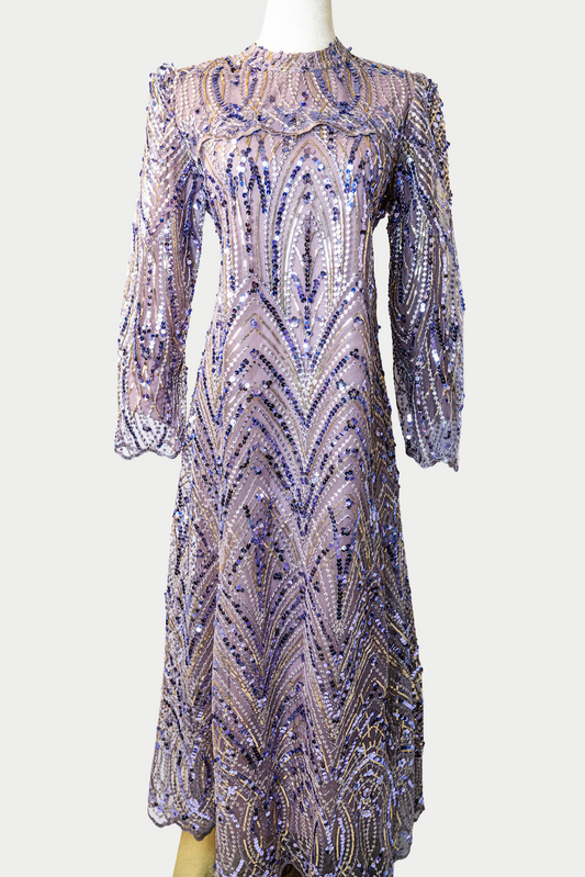 A stunning long dress in purple with sequins and delicate embroidery. The dress has mandarin collar, long sleeves, and is fully lined. There are hidden zips at the back and sleeves for ease of wear. The design is hijabi-friendly for modesty and style. It also includes a size-adjustable belt for a customized fit.