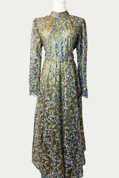 A stunning long dress in dark green with sequins and delicate golden embroidery. The dress has mandarin collar, long sleeves, and is fully lined. There are hidden zips at the back and sleeves for ease of wear. The design is hijabi-friendly for modesty and style. It also includes a size-adjustable belt for a customized fit.