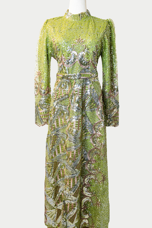 A stunning long dress in green with sequins and delicate golden embroidery. The dress has mandarin collar, long sleeves, and is fully lined. There are hidden zips at the back and sleeves for ease of wear. The design is hijabi-friendly for modesty and style. It also includes a size-adjustable belt for a customized fit.