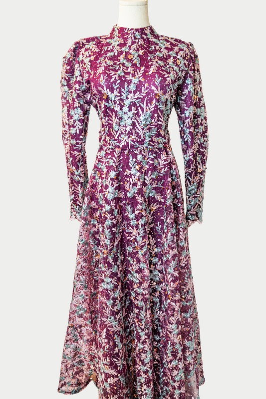 A stunning long dress in purple with sequins and delicate golden embroidery. The dress has mandarin collar, long sleeves, and is fully lined. There are hidden zips at the back and sleeves for ease of wear. The design is hijabi-friendly for modesty and style. It also includes a size-adjustable belt for a customized fit.