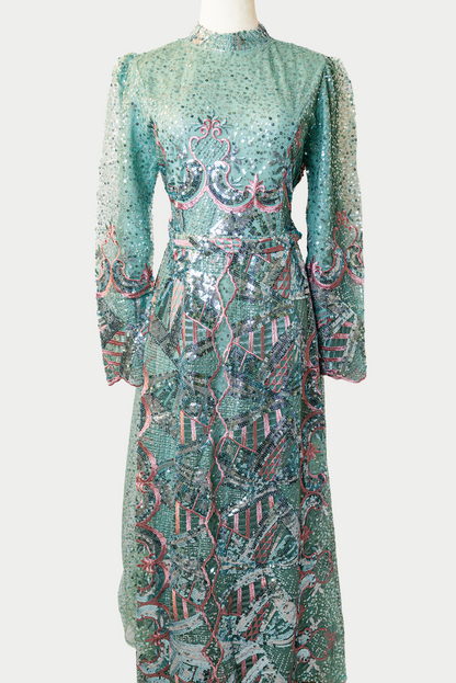 A stunning long dress in green with sequins and delicate pink embroidery. The dress has mandarin collar, long sleeves, and is fully lined. There are hidden zips at the back and sleeves for ease of wear. The design is hijabi-friendly for modesty and style. It also includes a size-adjustable belt for a customized fit.