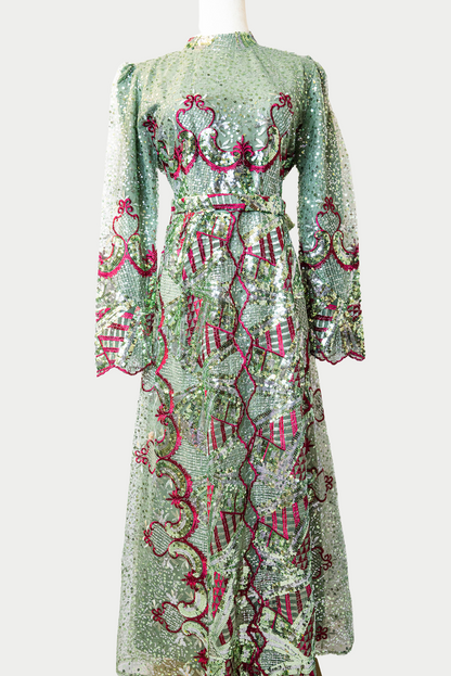 A stunning long dress in green with sequins and delicate red embroidery. The dress has mandarin collar, long sleeves, and is fully lined. There are hidden zips at the back and sleeves for ease of wear. The design is hijabi-friendly for modesty and style. It also includes a size-adjustable belt for a customized fit.